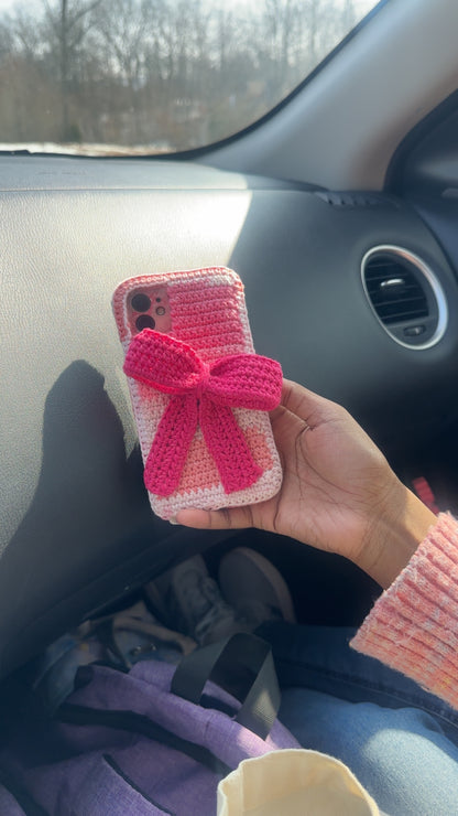 Hand holding a pink crocheted phone case with a bow in a car.