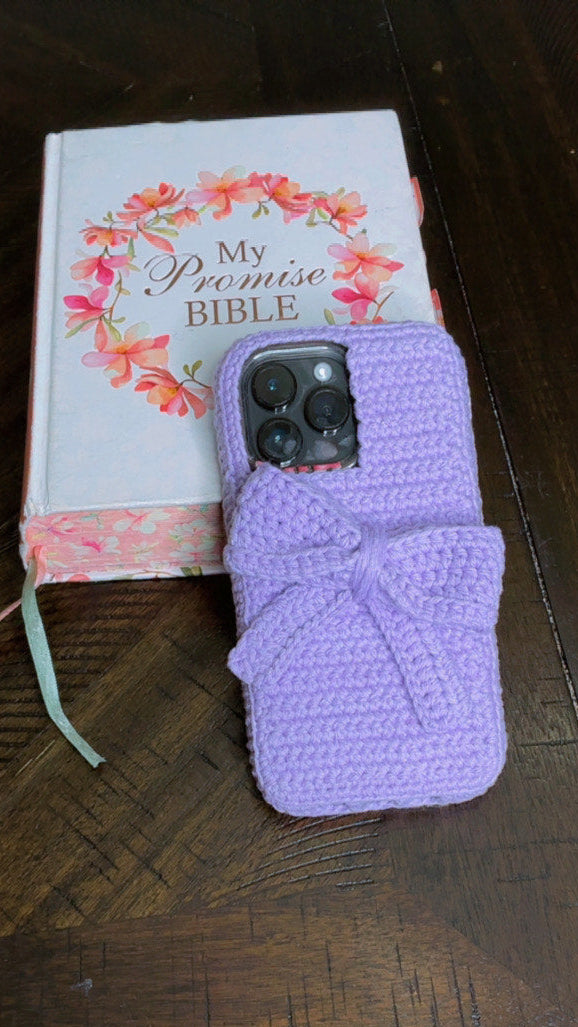 Purple crocheted phone case on a wooden surface with a book titled 'My Promise Bible' in the background.