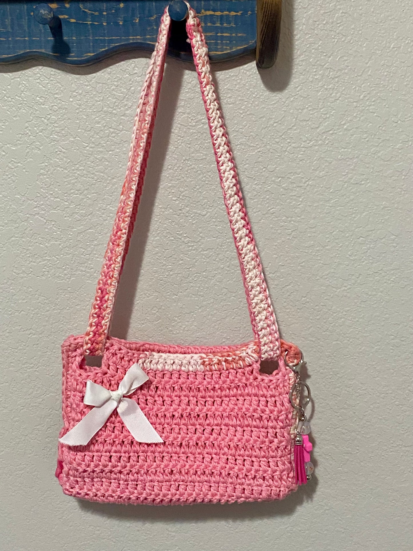 Pink crocheted handbag with a white bow and keychain.